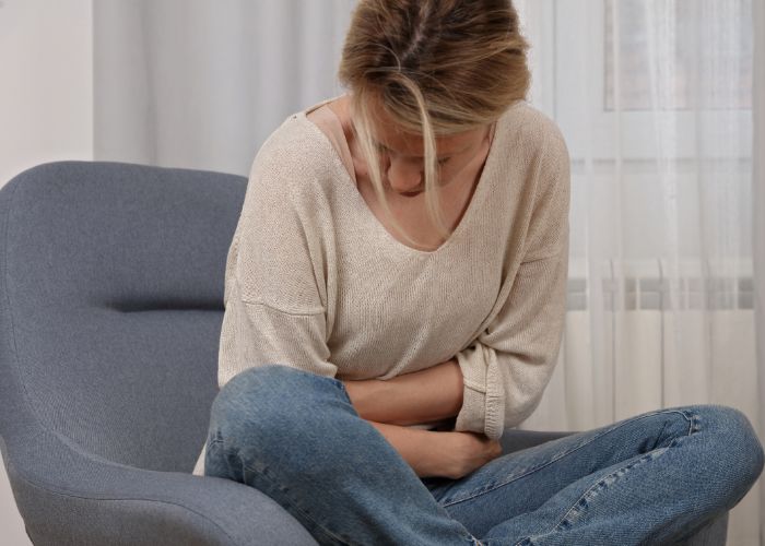 Frau sitzt mit Bauchschmerzen auf Sessel und hält sich den Bauch