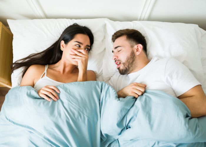 Frau hält sich Mund zu, weil Mann im Bett Mundgeruch hat