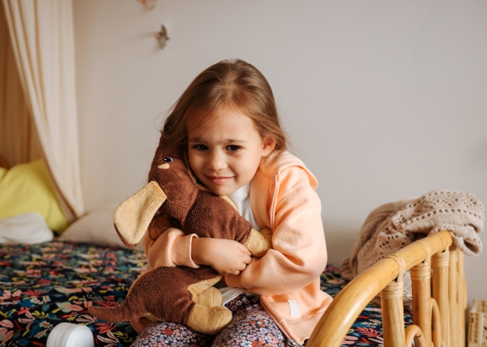 Niña pequeña sosteniendo un osito de peluche con cara de malestar, representando el estrés infantil y sus efectos en la salud digestiva.